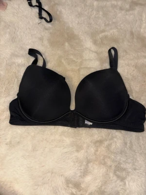 Svart vadderad bh med bygel - En klassisk svart bh med vadderade kupor och bygel för extra stöd. Justerbara axelband och hakknäppning bak. Slät design som passar under de flesta plagg. Materialet känns mjukt och stretchigt mot huden.