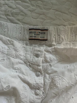 Vit broderad kjol Holly & Whyte - Säljer en vit kjol från Holly & Whyte by Lindex med broderade blommor och hålmönster. Kjolen har knappar framtill och är gjord i ett lätt bomullstyg, perfekt för varma dagar. Supersöt och enkel att styla till olika toppar! Säljer på grund av att den är för liten 