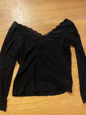 Svart topp med spetsdetalj - Snygg svart långärmad topp med v-ringning och spetsdetalj längs halsringningen.