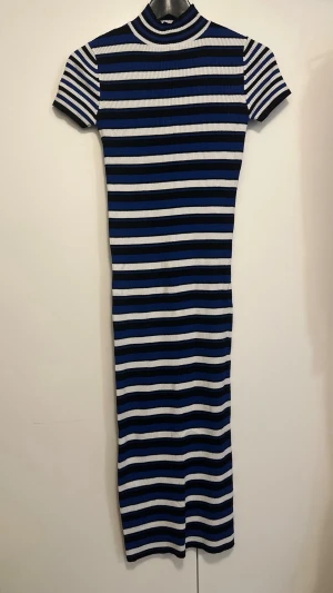 Randig ribbad klänning från Zara - Säljer en ribbad, kroppsnära klänning från Zara med blå, svarta och vita horisontella ränder. Klänningen har korta ärmar, hög hals och är i stretchigt stickat material. 