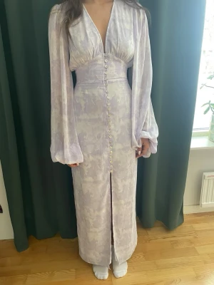 Adoore lila Positano dress💜 - Magiskt fin maxiklänning i ljus lavendel med romantiska detaljer. Djup V-ringning, markerad midja och knappar framtill. Långa puffärmar som ger en exklusiv och feminin känsla.  Perfekt till student, bröllop, midsommar, sommarfest eller middag 🫶  Använd 2 gånger, mycket fint skick.