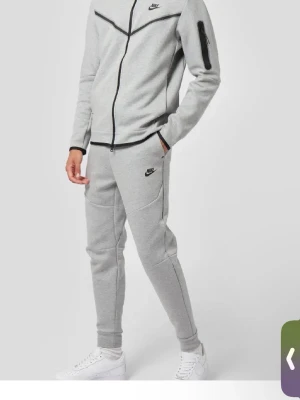 Grå mjukisbyxor från Nike - Snygga grå mjukisbyxor från Nike med svart logga på låret. Byxorna har en slim fit-modell, resår i midjan och muddar vid bensluten. Perfekta för chill eller träning, med bekvämt och mjukt material.