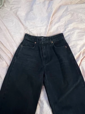 Svarta vida jeans med hög midja - Säljer ett par svarta jeans med hög midja och raka, vida ben. Jeansen har klassisk femficksdesign och bälteshällor. Perfekta för en avslappnad och trendig stil. Materialet är kraftig denim i bomull.