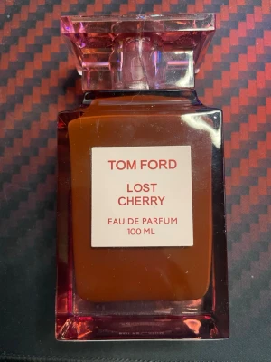 Tom Ford Lost Cherry EdP 100 ml - Tom Ford Lost Cherry Eau de Parfum i en lyxig, fyrkantig glasflaska med rödrosa ton och elegant etikett. Flaskan rymmer 100 ml och har en distinkt, tung kork. Perfekt för dig som gillar exklusiva och fruktiga dofter.