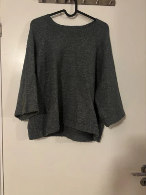 Grön trekvartsärmad stickad tröja - Mysig grön stickad tröja med bred halsringning och vida trekvartsärmar. Tröjan har en fin passform och är inte för lång. Den sticks inte och är använd fåtal gånger. Färgen är lite blågrön.