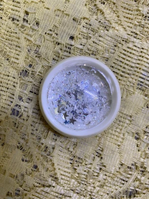Nageldekoration glitter stjärnor - Nageldekoration i form av glitter med holografiska stjärnor och små flakes i silver och transparent. Perfekt för att skapa unika och glittriga nageldesigner. Kommer i en liten rund plastburk.