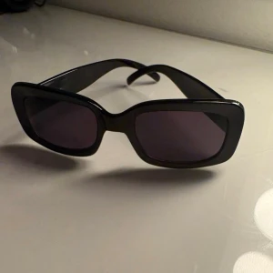 Svarta rektangulära solglasögon - Snygga svarta solglasögon med rektangulära bågar och mörka glas. Klassisk och stilren design som passar till de flesta outfits. Mormors gamla, ändå väldigt fint skick 