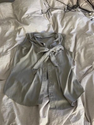 Calvin klein blus - Vintage Grey Calvin Klein Sleeveless Blouse – Chic & Elegant  Elevate your wardrobe with this vintage grey Calvin Klein blouse. Featuring a delicate button-down front that meets in a stylish bow at the top, and a subtle neckline that adds a touch of sophistication. Made from lightweight, airy fabric, this sleeveless design is perfect for a chic, effortless look.  A timeless piece for a polished, elegant outfit!