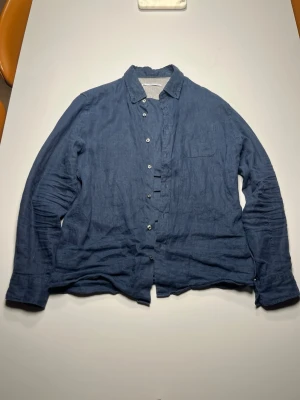 Blå linneskjorta med knappar - Säljer en blå skjorta i linne med klassisk krage och knappar framtill. Skjortan har långärmad design och en bröstficka. Perfekt för dig som gillar en avslappnad och stilren look.