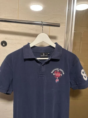 Mörkblå pikétröja Nautical Center - Mörkblå pikétröja från Everest med broderad Nautical Center-logga på bröstet och stora siffror 86 på ärmen. Klassisk krage och korta ärmar, tillverkad i bomull för en bekväm känsla.