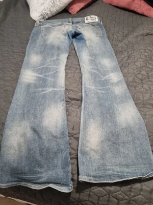 Blåa bootcut jeans Cheap Monday - Säljer ett par ljusblå bootcut jeans från Cheap Monday med slitna detaljer och två bakfickor. Jeansen har en klassisk femficksmodell och ett stort vitt Cheap Monday-märke bak i linningen. Perfekta för dig som gillar retrostil och breda ben. Använd fåtal gånger storlek 34/32