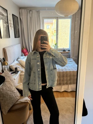 Ljusblå jeansjacka med stora fickor - Säljer en ljusblå jeansjacka med klassisk krage och stora, fyrkantiga fickor framtill. Jackan har raka ärmar och knäppning med silverfärgade knappar. Perfekt för dig som gillar en avslappnad och trendig look. Super trendig jacka 
