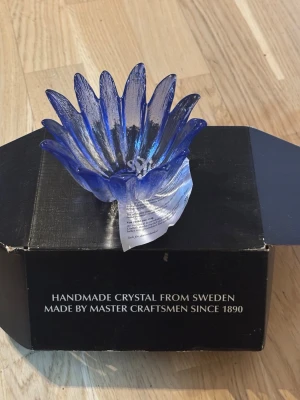 Blå kristallskål från Målerås - Unik handgjord kristallskål från Målerås, formad som en blomma med blå och klara detaljer. Skålen är tillverkad i Sverige av skickliga hantverkare och levereras i originalförpackning. Perfekt som dekoration eller present.