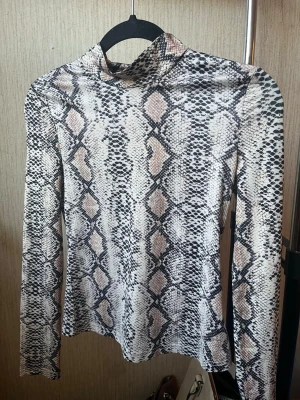 Polotopp med ormmönster - Snygg polotopp med ormmönster i svart, beige och grå toner. Långärmad och figurnära passform. Tunt och stretchigt material.
