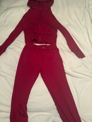 Vinrött loungewear-set med hoodie - Mysigt vinrött loungewear-set med croppad hoodie och matchande byxor med dragsko i midjan. Hoodien har dragkedja och långa ärmar, byxorna är mjuka och har avslappnad passform. Perfekt för chill dagar hemma.