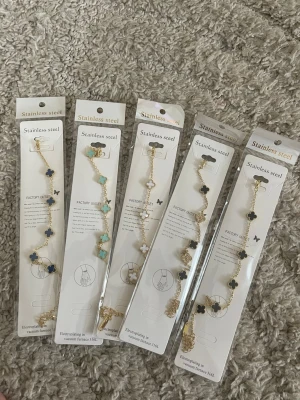 5st Guldpläterad armband med fyrklöver i stål - Snygga armband i rostfritt stål med guldfärgad kedja och pärlliknande fyrklöverhängen i olika färger som blått, turkost och vitt. Perfekt accessoar för att lyfta din outfit med en trendig och elegant touch.