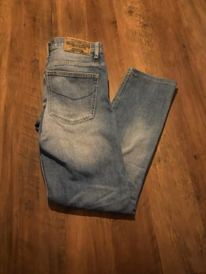 Blå raka slim jeans från Crocker jeans  - Klassiska blå jeans från Crocker Jeans i modellen 310 slim med raka ben och normal passform. Jeansen har en ljus tvätt med snygga slitningar på låren och är tillverkade i robust denim. Perfekta för en avslappnad och tidlös stil. Dom är i bra skick med det finns ett litet hål längst ner på ett utav benen(se bild).