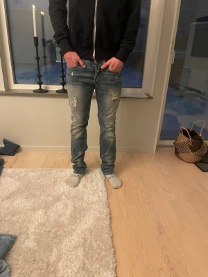 Replay jeans med slitningar  - Tja säljer ett par riktigt snygga och archive jeans från replay. ett par blå jeans från replay med snygga slitningar och ljusa tvättade partier. Jeansen har klassisk femficksdesign, raka ben och läderpatch bak i midjan. Perfekta för en avslappnad och trendig look. På bilden ser de ut som att de e bootcut men tror ej de är de eftersom de är för små i midjan för mig och för långa som gör att de ser ut som de! Skick 10/10 storlek 31/34 jag är 183! Hör av dig vid mer frågor🤩mvh PREMIUM FASHION🙌🏼