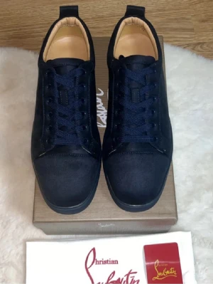 Marinblå sneakers från Louboutin - Snygga marinblå sneakers från Christian Louboutin med klassisk röd sula och diskret logga. Skorna har en låg profil, rund tå och är tillverkade i textil med matchande blå skosnören. Perfekta för dig som vill ha en stilren och exklusiv look.