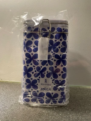Mon Amie Blåvit plåtburk Rörstrand x Zoégas EFTERTRAKTAD 🌟 - Passa på och köp denna eftertraktade burk utan frakt. Snygg plåtburk i vitt med blått blommönster Mon Amie från Rörstrand i samarbete med Zoégas. Burken har ett tättslutande lock med metallspänne och är perfekt för förvaring av kaffe eller te. Klassisk design som passar i de flesta kök. Oanvänd helt ny. 