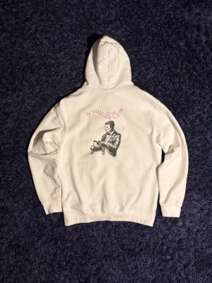 Vit hoodie Sommelier Club - Vit hoodie med huva och känguruficka från Sommelier Club. På bröstet finns en liten röd logga med en flaska och text, och på ryggen ett stort tryck av en sommelier med texten 'Sommelier Club'. Perfekt för dig som gillar stilrena och unika plagg. Den har lite fläckar som syns på bilden samt nopprig på insidan. Sitter som S mer. Hör av er vid minsta fundering!