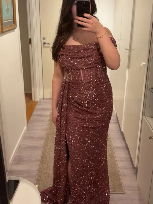 Glittrig rosa röd långklänning - Superfin vinröd långklänning med glittriga paljetter och offshoulder-design. Klänningen har en markerad midja, slits framtill och vackra draperingar över bysten. Perfekt för bal eller festliga tillfällen. Materialet känns lyxigt och skimrande. Det är storlek XL på klänningen men den funkar ungefär som M-L efter den är lite liten i storleken.❣️