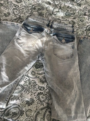 Ljusblåa lowwaist bootcut jeans med tvättad look - Säljer ett par ljusblåa low waist bootcut jeans med snyggt tvättad effekt och kontrastfärgade detaljer vid fickorna. Jeansen har fem fickor och breda ben, perfekta för en avslappnad och trendig stil. Klassisk knappgylf och bälteshällor.