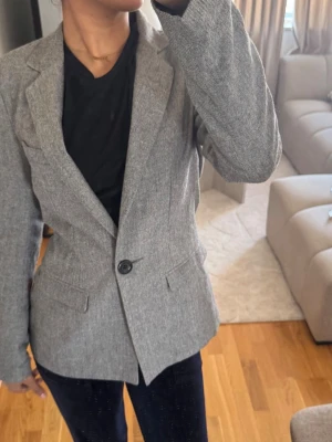Grå klassisk kavaj med enkel knapp - Snygg grå kavaj med figurnära passform och en knapp framtill. Kavajen har klassiska slag, två fickor med lock och är tillverkad i ett vävt material som ger en stilren look. Perfekt att matcha med både jeans och kostymbyxor.
