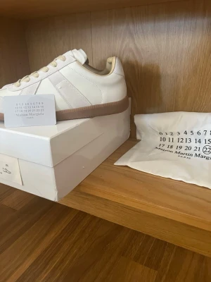 Maison Margiela vita sneakers - Maison Margiela sneakers i vitt läder och mocka med klassisk gummisula. Lågt skaft och vita snören. Ikonisk design med diskreta detaljer och stilren look. Perfekta för dig som gillar minimalistisk och clean stil. Kvitto finns!!!!