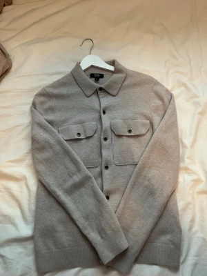 Beige overshirt från Reiss - Stilren beige overshirt från Reiss i 100% marinull. Klassisk krage, två bröstfickor med lock och knappar framtill. Perfekt lager-på-lager-plagg. Nypris 1500kr  