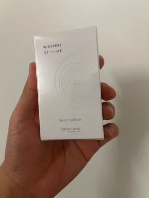 HELT NY! Oriflame Whispers of Me Eau de Parfum  - Oöppnade Minimalistisk parfym från Oriflame med namnet Whispers of Me. Förpackningen är vit med subtila grafiska linjer och svart text. Rektangulär kartong i papper som ger en stilren och modern känsla. Perfekt för dig som gillar eleganta och diskreta dofter.