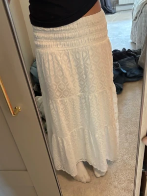 Vit långkjol med strukturmönster strl 146/152 från Gina Tricot  - Säljer en vit långkjol med bred resår i midjan och ett diskret strukturmönster. Kjolen har volangdetaljer och är luftig, perfekt för varmare dagar. Passar till både sneakers och sandaler för en chill look.