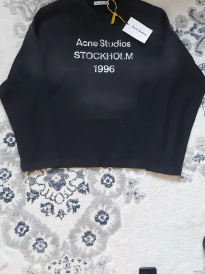 Svart långärmad topp Acne Studios - Medium. Cool svart långärmad topp från Acne Studios med trycket 'Acne Studios STOCKHOLM 1996' på bröstet. Klassisk passform och rund halsringning. Perfekt för dig som gillar stilrena och trendiga plagg från populära märken.