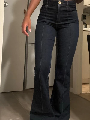 Mörkblå utsvängda jeans med hög midja - Snygga mörkblå jeans med hög midja och utsvängda ben. Jeansen har markerade sömmar framtill och klassisk femficksdesign. Perfekta för dig som gillar en trendig och bekväm stil.