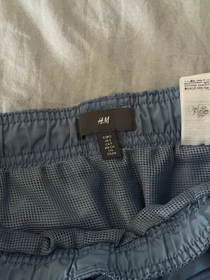 Blå shorts från H&M med meshfoder - Säljer ett par blå shorts från H&M i storlek S. Shortsen har elastisk midja och meshfoder på insidan för extra komfort. Perfekta för varma dagar eller träning. Klassisk design utan synliga loggor på utsidan.