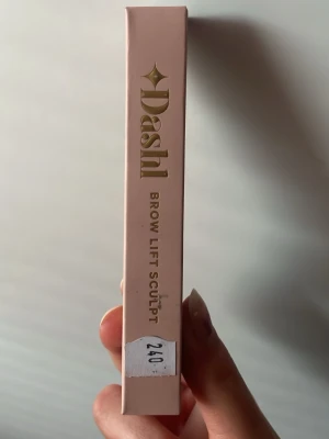 Dashl Brow Lift Sculpt ögonbrynspenna - Dashl Brow Lift Sculpt är en ögonbrynspenna i ljusrosa hylsa med guldfärgad text. Pennan har en svart borste/kam i plast för att forma och lyfta brynen. Perfekt för att skapa definierade och stylade ögonbryn med precision.