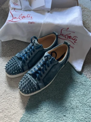 Blåa Louboutin sneakers med nitar - Säljer ett par blåa sneakers från Christian Louboutin med coola metallnitar på tån. Skorna har blå mocka, matchande blå skosnören och vit sula. Perfekta för dig som vill sticka ut med en edgy och lyxig stil. Dust bags låda extra spikar och kvitto finns!, köpt i Christian Louboutins butik i Danmark 