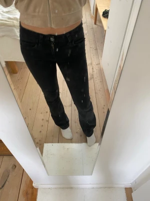 Svarta bootcut jeans med fickor - Säljer ett par svarta bootcut jeans med klassisk femficksdesign och knappgylf. Jeansen har en något utsvängd passform nedtill och är tillverkade i ett stretchigt denimtyg som sitter snyggt på kroppen. Perfekta till en avslappnad och trendig look. Storlek 164