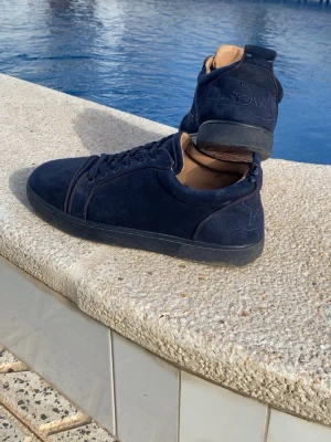 Mörkblå sneakers från Louboutin - Christian Louboutin Sneakers – Mörkblå Mocka  Säljer ett par snygga och exklusiva Christian Louboutin sneakers i mörkblå mocka. Skorna är använda men fortfarande väldigt stilrena och bekväma.  Skick:  * Normalt slitage på de röda sulorna. * Mindre märken och smuts på mockan. * Något slitage på kanter och sulor. * Inga större skador som påverkar användningen. * Skadorna/slitaget går att åtgärda hos skomakare eller med rätt skovård om man vill få dem i ännu bättre skick. Hör av er vid frågor  