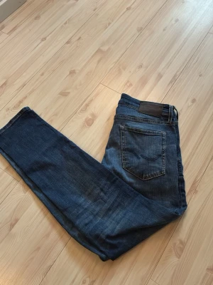 Mörkblå raka jeans med slitningar - Snygga mörkblå jeans med raka ben och diskreta slitningar. Klassisk femficksmodell med kontrastsömmar och läderpatch bak i midjan. Jeansen har en cool tvättad look och passar perfekt till en avslappnad stil.