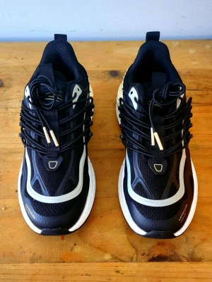 Svarta chunky Philipp Plein sneakers med gulddetaljer - Snygga svarta Philipp Plein sneakers med vita och grå detaljer samt guldfärgade inslag på sulan. Skorna har en chunky sula, mesh- och syntetmaterial, och coola snörningar med metalltips. Perfekta för dig som vill sticka ut med din streetstyle.