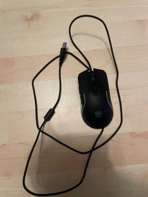 SG Station Gear gamingmus USB - Säljer en svart gamingmus från SG Station Gear med USB-anslutning. Musen har ergonomisk form, flera knappar och en lång kabel för smidig användning. Perfekt för gaming eller arbete vid datorn.