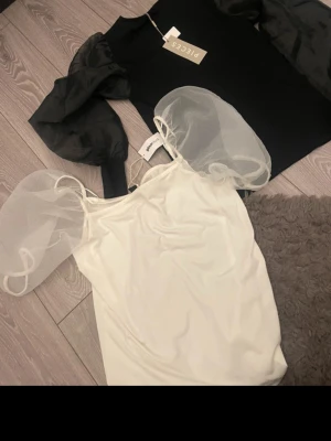 Svart topp med puffärmar från Pieces - Trendig svart topp från Pieces med transparenta puffärmar i mesh som ger en cool kontrast till den enkla kroppen. Rund halsringning och normal passform. Perfekt för dig som vill sticka ut lite extra.