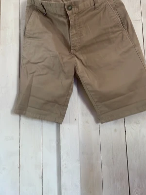 Beige shorts från Berkeley - Säljer ett par klassiska beige shorts från Berkeley. De har normal passform, sidofickor och stängs med knapp och dragkedja. Perfekta för varma dagar och enkla att matcha med olika stilar.