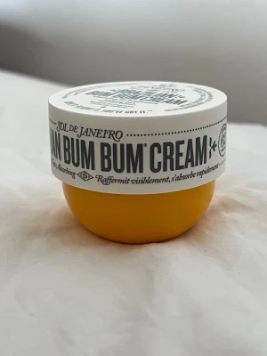 Sol de Janeiro Bum Bum Cream - Sol de Janeiro Brazilian Bum Bum Cream i en rund, gul burk med vitt lock. En ikonisk kroppskräm med doft av pistage och salt karamell, känd för sin återfuktande och uppstramande effekt. Perfekt för dig som vill ha silkeslen hud och en tropisk känsla.