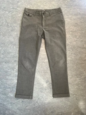 Grå kostymbyxor Dressmann Slim Fit - Snygga grå kostymbyxor från Dressmann i modellen Slim Fit. Byxorna har klassisk design med bälteshällor, knapp och dragkedja framtill samt uppvikta benslut. Perfekta för en stilren look.  #Dressmann #Kostymbyxor #GråKostymbyxor #SlimFit #Herrmode #BusinessCasual #KlassiskStil #Stilren #Formellt #SecondHand #Begagnat #Herrkläder