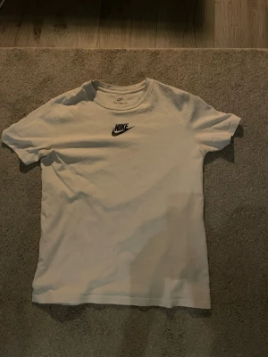 Vit Nike t-shirt med logga - Klassisk vit t-shirt från Nike med svart logga tryckt på bröstet. T-shirten har rund halsringning och korta ärmar. Tillverkad i mjuk bomull för en skön och avslappnad stil. Perfekt basplagg för alla tillfällen. Loose fit.