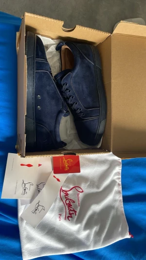 Mörkblå sneakers från Louboutin - Snygga mörkblå sneakers från Christian Louboutin i mocka med klassiska röda sulor och diskreta detaljer. Skorna har lågt skaft, svarta snören och en stilren design som passar till det mesta. Kommer med originalpåse och certifikat.