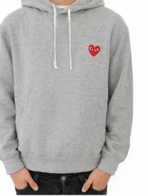 Grå hoodie Comme des Garçons Play - Säljer en grå hoodie från Comme des Garçons Play med det ikoniska röda hjärtat med ögon broderat på bröstet. Hoodien har huva med vit dragsko och en stor magficka. Tillverkad i mjukt bomullsmaterial som är perfekt för en avslappnad stil. Nypris ligger på 2499. Passar folk mellan 160 till 175 cm beroende på vikt samt hur du föredrar att den ska sitta.