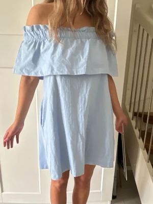 Ljusblå offshoulder klänning - Söt ljusblå kortklänning med offshoulder-design och volang upptill. Klänningen har en avslappnad passform och är perfekt för varma dagar. Tillverkad i ett lätt bomullstyg som känns skönt mot huden. Den har även två fickor på sidorna men de ”smälter in” i klänningen. Sälja inte längre! Storleken är 36. Aldrig använt den.